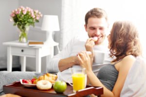 Picture of young couple eating breakfast in bed